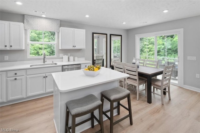 kitchen with dishwasher, a center island, white cabinets, sink, and light wood-type flooring