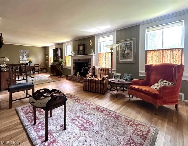 living room with wood-type flooring, ornamental molding, and a brick fireplace