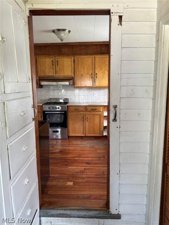 kitchen featuring hardwood / wood-style floors, backsplash, wood walls, and stainless steel gas range