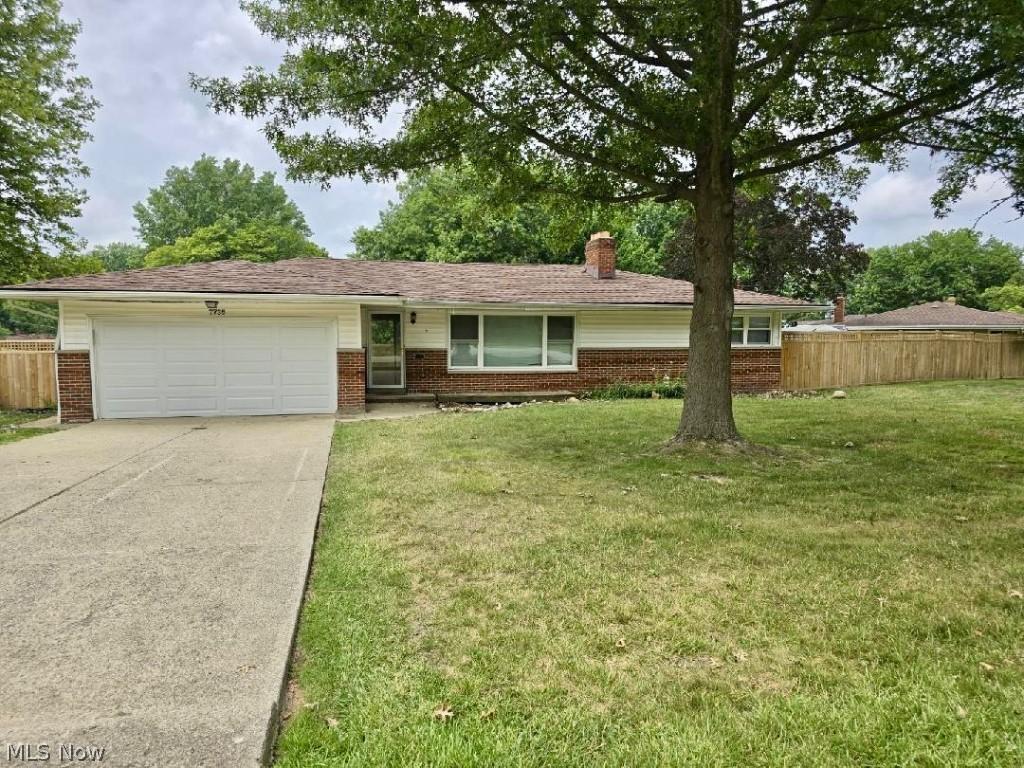 ranch-style house with brick siding, fence, a garage, driveway, and a front lawn