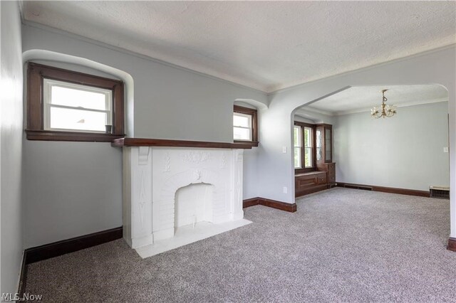 unfurnished living room with carpet flooring, ornamental molding, a textured ceiling, and a notable chandelier