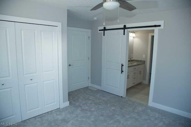 unfurnished bedroom with carpet flooring, a barn door, a closet, and ceiling fan