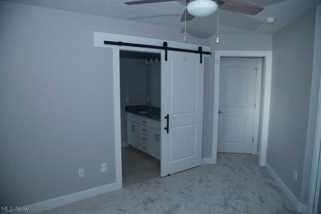 unfurnished bedroom with ceiling fan, a barn door, light colored carpet, and sink