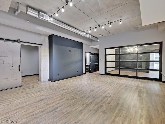 empty room with a barn door, track lighting, a high ceiling, and light hardwood / wood-style flooring