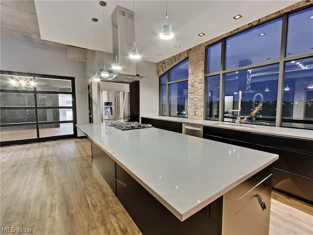 kitchen featuring appliances with stainless steel finishes, island range hood, hanging light fixtures, a kitchen island, and light wood-type flooring