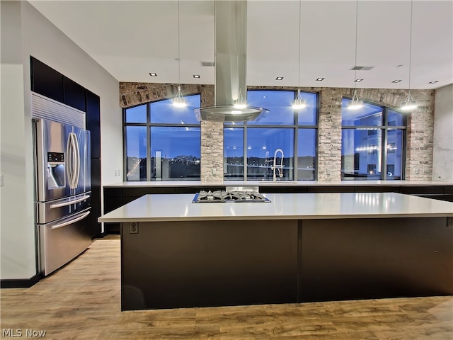 kitchen with appliances with stainless steel finishes, decorative light fixtures, light wood-type flooring, island exhaust hood, and a center island