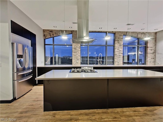 kitchen featuring stainless steel appliances, light hardwood / wood-style flooring, decorative light fixtures, sink, and island exhaust hood