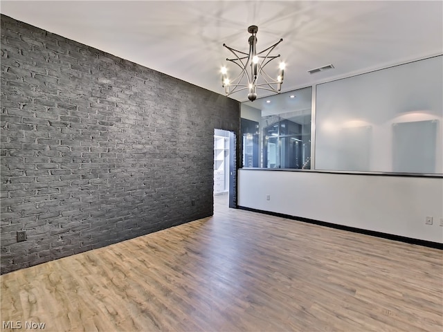 spare room featuring wood-type flooring, brick wall, and a chandelier