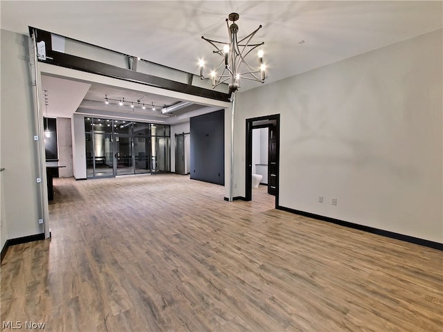 unfurnished living room with an inviting chandelier, track lighting, and hardwood / wood-style floors