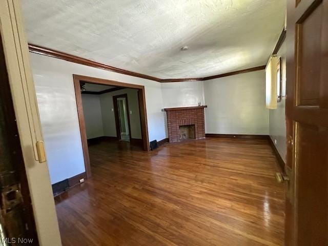 unfurnished living room featuring hardwood / wood-style floors, ornamental molding, a textured ceiling, and a brick fireplace