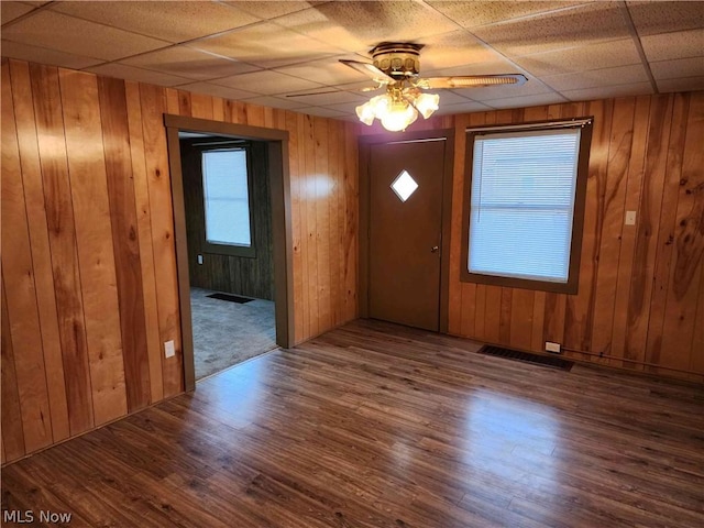 foyer with wood-type flooring, wooden walls, ceiling fan, and a paneled ceiling