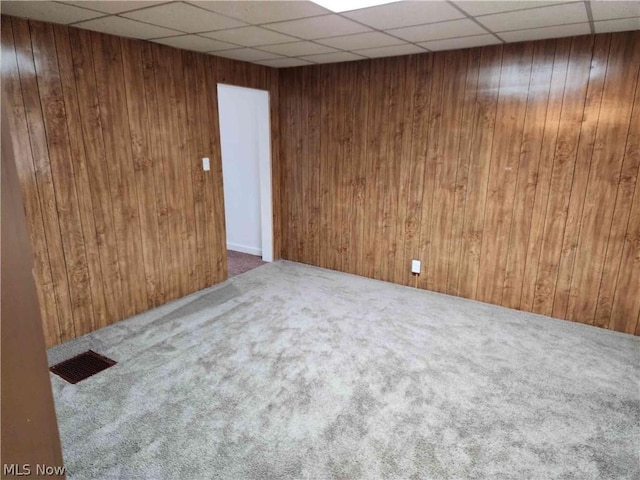 carpeted empty room featuring a drop ceiling and wood walls