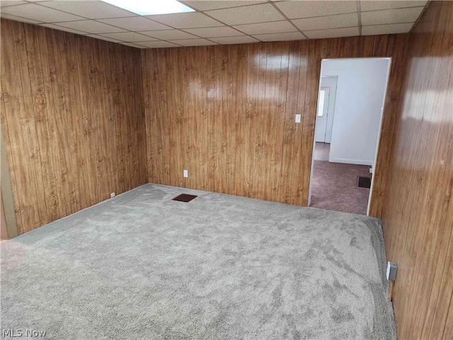 unfurnished room with wooden walls, a drop ceiling, and dark colored carpet