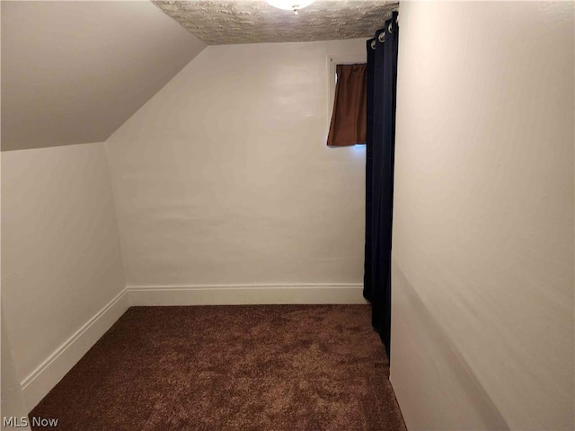 additional living space featuring lofted ceiling and dark colored carpet