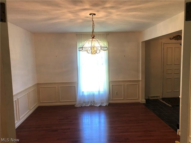 unfurnished dining area with dark hardwood / wood-style floors and an inviting chandelier