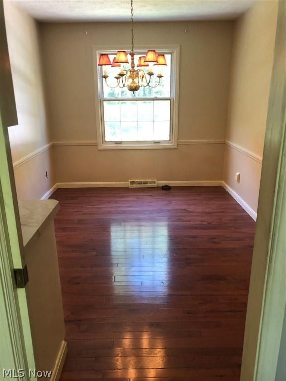 empty room featuring a notable chandelier and dark hardwood / wood-style floors