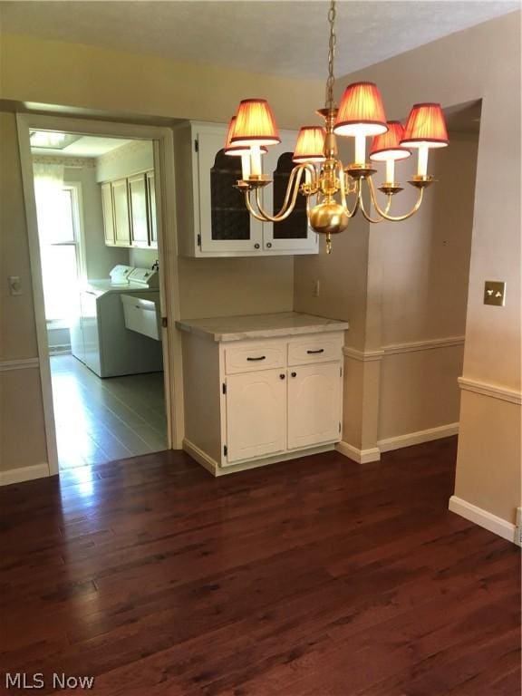 unfurnished dining area featuring dark hardwood / wood-style floors, washer and dryer, and an inviting chandelier