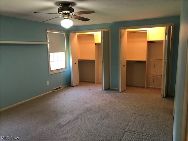 unfurnished bedroom featuring ceiling fan, light colored carpet, and two closets