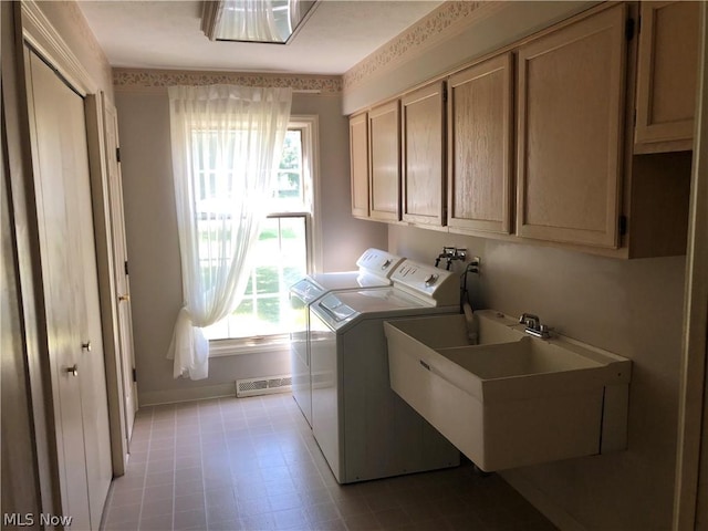 clothes washing area with washing machine and clothes dryer, cabinets, sink, and a healthy amount of sunlight