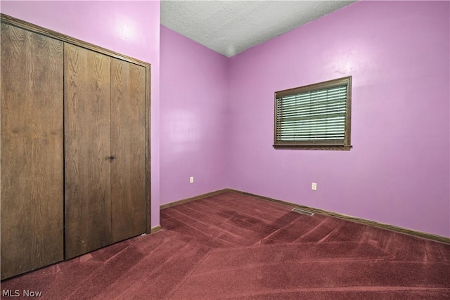 unfurnished bedroom with a closet, dark carpet, and a textured ceiling