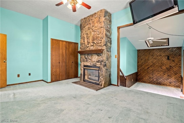 unfurnished living room featuring light colored carpet, a stone fireplace, ceiling fan, and wood walls