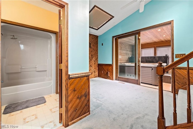 interior space featuring ceiling fan,  shower combination, wooden walls, and vaulted ceiling