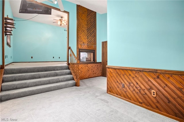 stairs with a multi sided fireplace, carpet floors, ceiling fan, and wooden walls