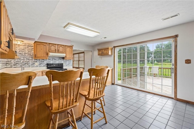 kitchen with sink, tasteful backsplash, a breakfast bar, light tile patterned floors, and range