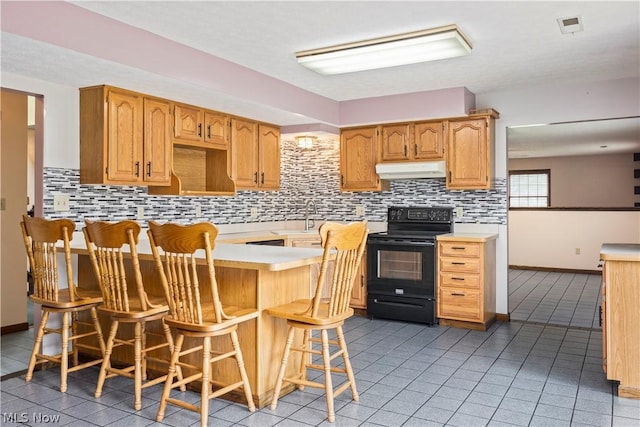 kitchen with backsplash, light tile patterned floors, black / electric stove, a kitchen bar, and kitchen peninsula