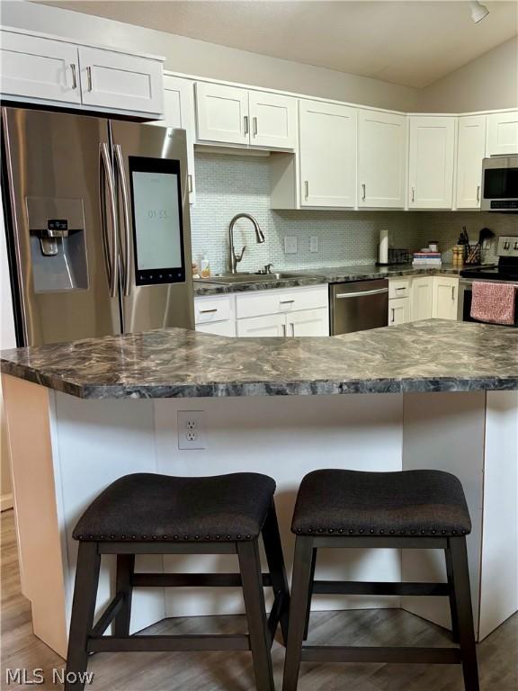 kitchen featuring a breakfast bar, sink, stainless steel appliances, decorative backsplash, and white cabinets