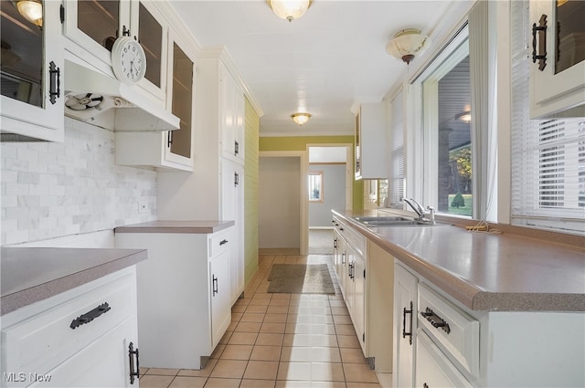 kitchen featuring decorative backsplash, ornamental molding, sink, light tile patterned floors, and white cabinetry