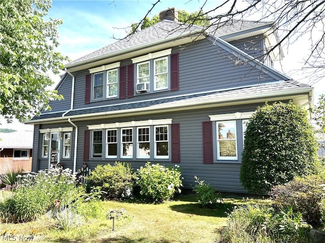 view of front facade with roof with shingles, a chimney, and a front yard