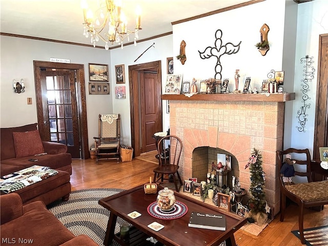 living room featuring a notable chandelier, a brick fireplace, crown molding, and wood finished floors