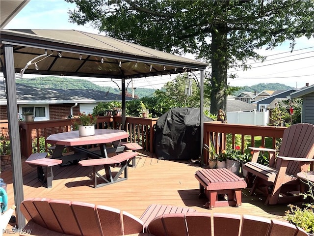 wooden terrace with a gazebo, fence, grilling area, and outdoor dining space