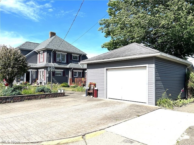 view of front of house featuring driveway, a shingled roof, a chimney, and an outdoor structure