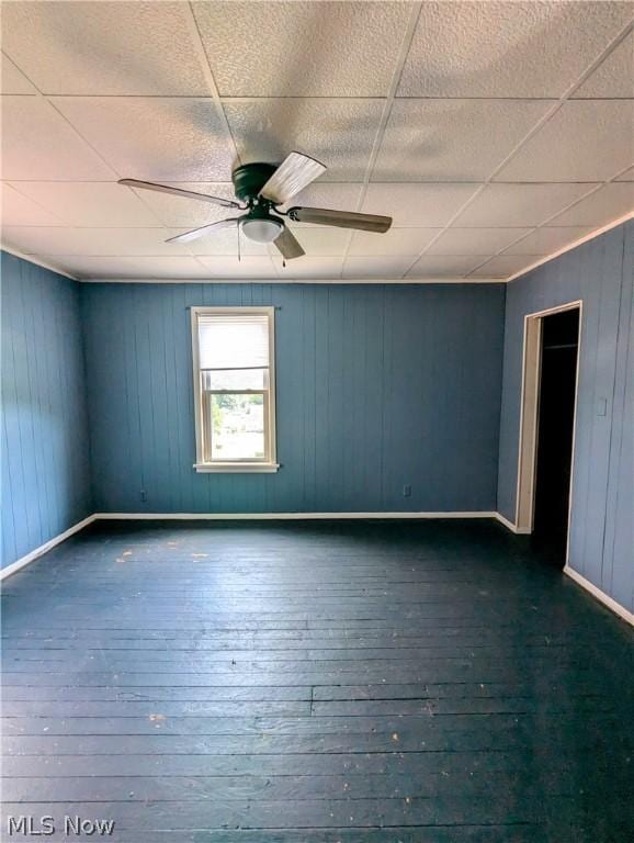 unfurnished room featuring a paneled ceiling, ceiling fan, wood walls, and dark hardwood / wood-style floors