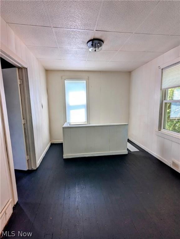 spare room with dark hardwood / wood-style floors, a drop ceiling, and a wealth of natural light