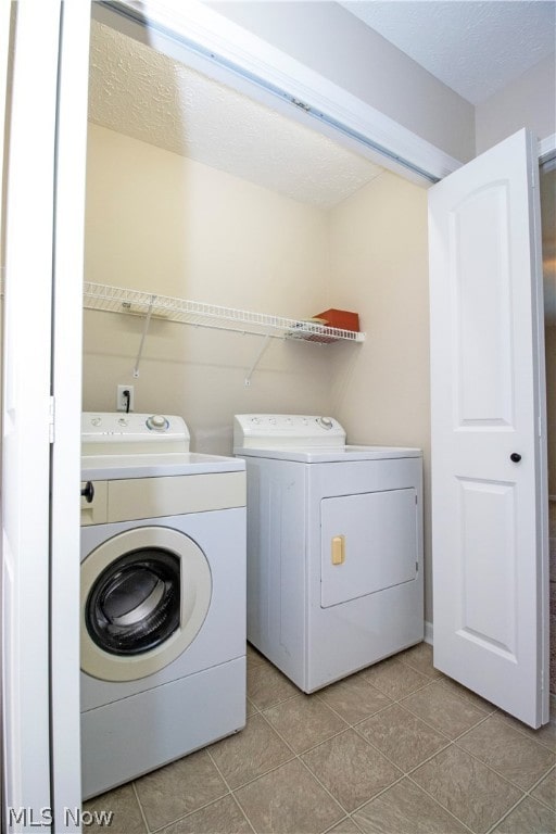 clothes washing area featuring laundry area, light tile patterned flooring, independent washer and dryer, and a textured ceiling