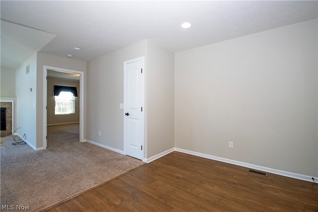 empty room with a tile fireplace, visible vents, baseboards, and wood finished floors