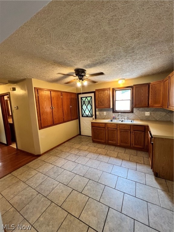 kitchen featuring tasteful backsplash, sink, light wood-type flooring, a textured ceiling, and ceiling fan