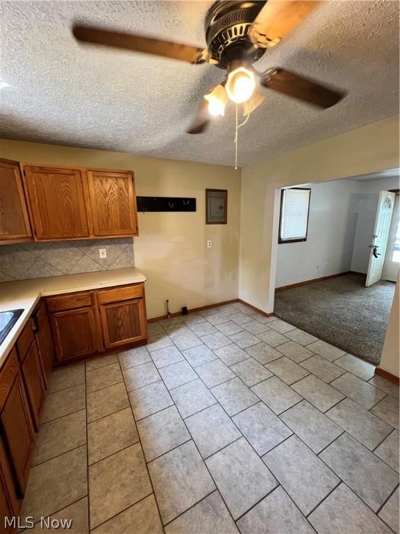 kitchen featuring backsplash, light tile patterned floors, a textured ceiling, electric panel, and ceiling fan