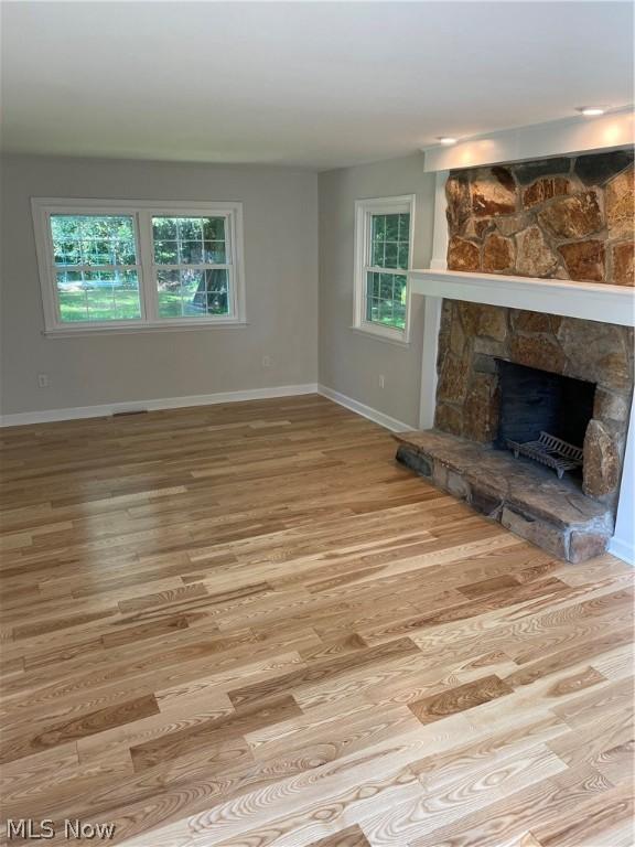 unfurnished living room featuring light wood-type flooring, a stone fireplace, and a wealth of natural light