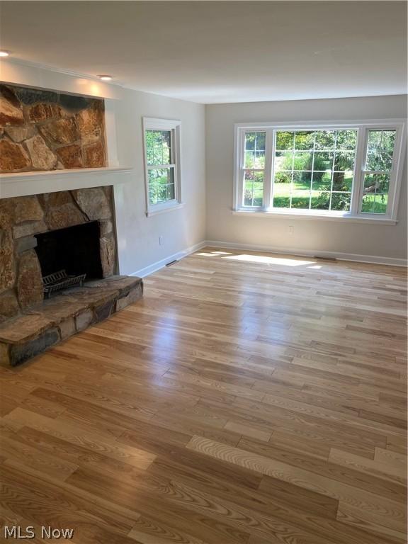 unfurnished living room with a stone fireplace and light wood-type flooring