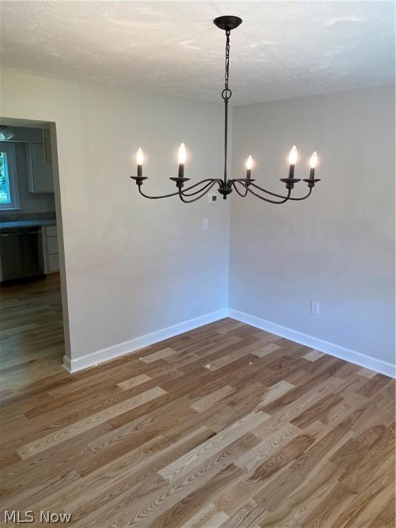 unfurnished dining area with wood-type flooring and a notable chandelier