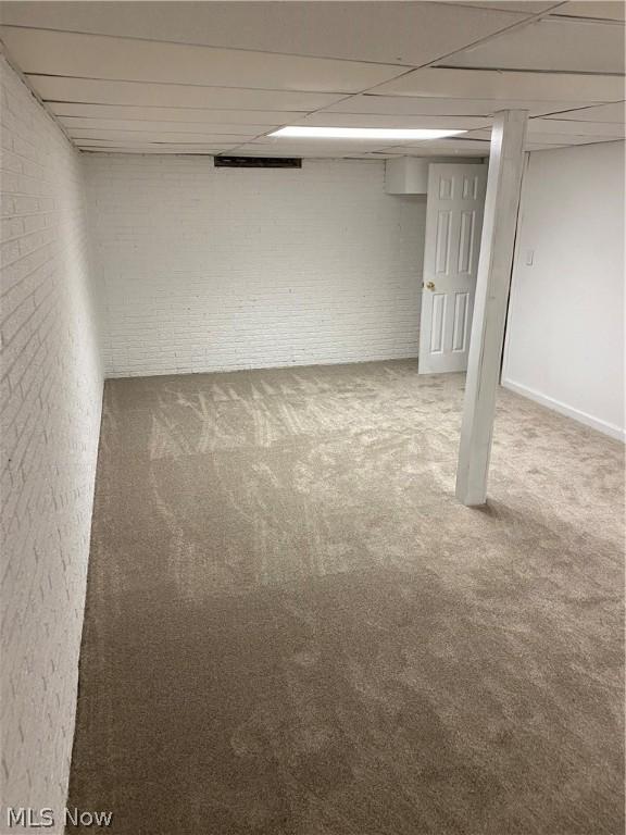 basement featuring carpet, a drop ceiling, and brick wall