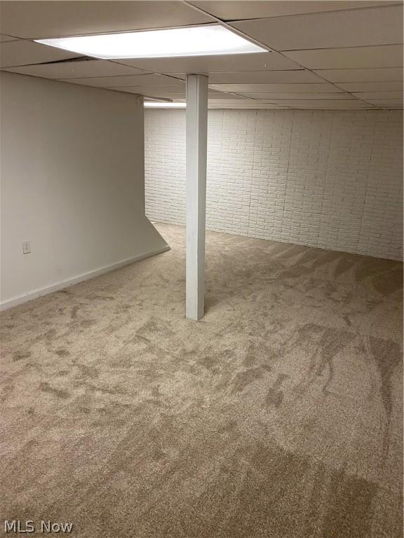 basement featuring carpet, a drop ceiling, and brick wall