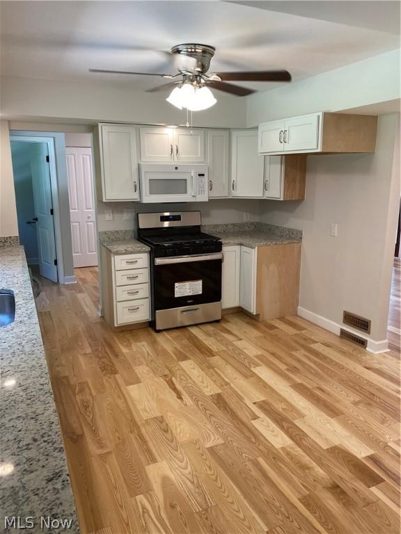 kitchen featuring white cabinets, light hardwood / wood-style floors, light stone counters, and stainless steel gas range