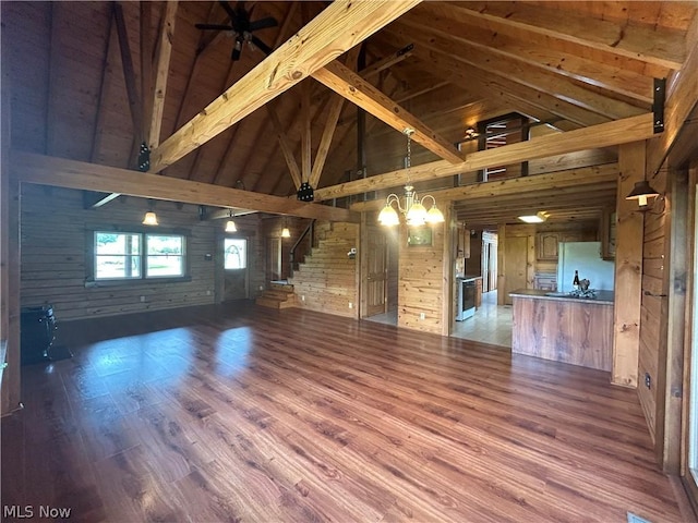 unfurnished living room featuring beamed ceiling, high vaulted ceiling, wooden walls, hardwood / wood-style flooring, and ceiling fan with notable chandelier