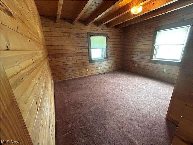 carpeted empty room with beamed ceiling and wood walls