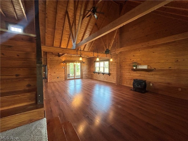 unfurnished living room with wooden walls, beamed ceiling, wooden ceiling, a wood stove, and wood finished floors